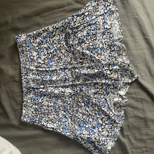 Blommig kjol i blått och vitt - Säljer en söt blommig kjol i blått och vitt med volangdetaljer. Kjolen har en kort längd och är perfekt för varmare dagar. Den har en bekväm passform och är lätt att matcha med olika toppar. Kjolen har inne shorts om man inte vill ha det är det bara att klippa bort