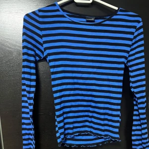 Blå och svart randig tröja - Säljer en blå och svart randig tröja med långa ärmar. Tröjan har en enkel design med en rund hals och är perfekt för en avslappnad stil. Den är tillverkad i ett mjukt och bekvämt material.