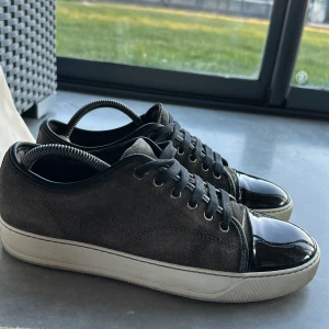 Bruna sneakers från Lanvin - Snygga bruna sneakers från Lanvin med svarta snören och en glansig svart tå. Perfekta för en stilren look. Säljer pga att de har blivit för små, storlek 40-41, dustbag medföljer 