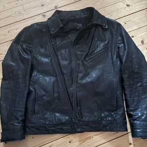 Svart skinnjacka från Filippa K Vintage - Snygg svart skinnjacka från Filippa K med dragkedja och en bröstficka med dragkedja. Jackan har en klassisk krage och långa ärmar. Jätte snygg och cool, är för män men har själv haft på mig den som tjej och den funkar toppen till båda ❤️Gammal och säljs inte längre, använd men i super bra skick. 