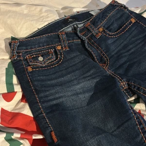 Jeans från True Religion - Snygga jeans från True Religion i en klassisk blå färg. De har en bootcut-stil och är midwaist. Jeansen har dekorativa sömmar och knappar på bakfickorna. Inte använda så mycket, inget slit. 