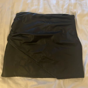 Svart kjol från Nelly - Snygg svart kjol från Nelly i ett glansigt material.  Storlek M Material med lite stretch i syntetiskt skinn Medelhög midja, rynkade detaljer i sidan, och omlottlagd design framtill Dragkedja i sidan Aldrig använd  Nypris 499kr  Vid frågor är det bara att höra av sig och priset går alltid att diskutera🙌🏻💞