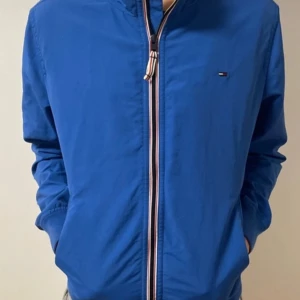 Blå vindjacka från Tommy Jeans 10/10 skick, använd kanske en gång  - Säljer en blå vindjacka från Tommy Jeans med dragkedja framtill och diskret logga på bröstet. Jackan har lång ärm och sportig känsla, perfekt för dig som gillar stilrena plagg med klassisk design.