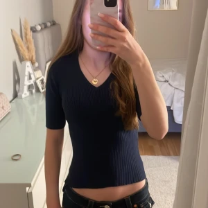 Mörkblå ribbad topp från Kappahl - Säljer en mörkblå ribbad topp från Kappahl med v-ringning och korta ärmar. Snygg och enkel modell som sitter figurnära och passar perfekt till jeans eller kjol.