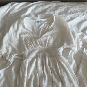 Vit omlottklänning från Amisu - Säljer en vit omlottklänning från Amisu med v-ringning och korta ärmar. Klänningen har markerad midja med bred resår och ett lätt plisserat tyg som ger en luftig känsla. Perfekt för sommarens alla tillfällen! ( finns också en knapp vid v-rigningen )