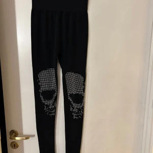 Svarta leggings med döskallemönster S/M - Svarta leggings med tight passform och coolt döskallemönster i silverfärgade nitar på knäna. Perfekta för dig som vill sticka ut med en edgy stil. Storlek S/M. Helt nya