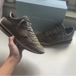 Beige sneakers från Philippe Model - Säljer ett par snygga beige sneakers från Philippe Model i mocka. Skorna har rund tå, snörning och en platt sula. Perfekta för dig som gillar stilrena och klassiska sneakers med en exklusiv känsla.strl 41 8/10 skick 