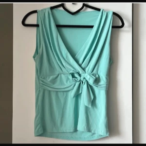 Turkos topp typ omlott - Söt turkos topp med omlott-effekt och knytning i midjan. Jätteskön att ha på sommaren. Funkar både till vardags och om man vill klä upp sig lite använd 1 gång, i väldigt bra skick. Köpt utomlands för 40eur så ca 400kr. Säljer då den inte kommit till användning.