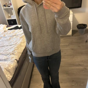 Grå hoodie med ficka - Säljer en klassisk grå hoodie med magficka och huva med dragsnören. Perfekt för en avslappnad stil och enkel att matcha med jeans eller andra byxor.