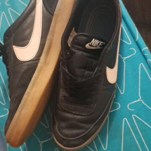 Svarta Nike sneakers med vit swoosh - Säljer ett par klassiska svarta Nike sneakers med vit swoosh och gummisula. Skorna har snörning och rund tå, perfekt för en sportig och stilren look. Passar både till vardags och träning.