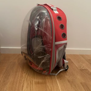 Katt-ryggsäck -  röd ryggsäck med transparent hårdplast på framsidan och flera ventilationshål. Väskan har justerbara axelremmar och meshfickor på sidorna. Aldrig använd