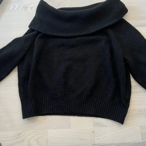 Svart stickad polotröja från H&M - Mysig svart stickad polotröja med bred krage för off shoulder och ribbade muddar. Perfekt för kyliga dagar och enkel att matcha med olika outfits.