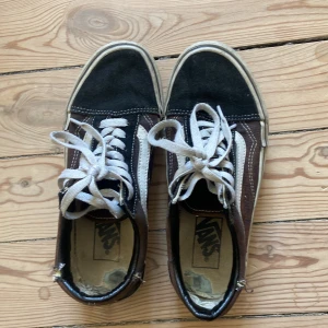 Vans Old Skool sneakers i svart - Klassiska Vans Old Skool sneakers med platå. Den svarta färgen är lite missfärgad på vissa ställen som skiftar i röda toner. Slitningar i hälpartiet och lite vid tåpartiet