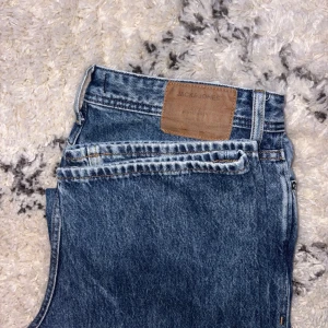 Blå jeans från Jack & Jones - Säljer ett par klassiska blå jeans från Jack & Jones med rak passform och normal midja. Jeansen har fem fickor, dragkedja och läderpatch bak i midjan. Perfekta till vardags för en avslappnad stil.