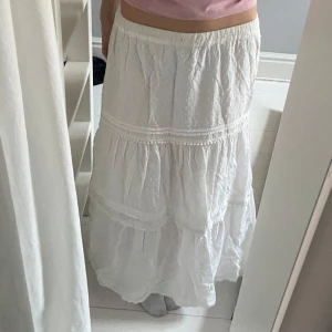 Vit långkjol med volanger - Säljer en vit långkjol med volangdetaljer och resår i midjan. I fint skick. Säljer då den tyvärr blivit lite för liten för mig som normalt bär S/M i underdelar och är 173 cm lång💗den har en liten fläck, antagligen från solkräm vid midjan som ej syns när man bär kjolen 