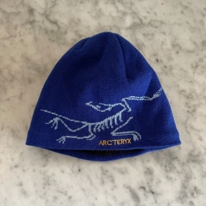 Blå mössa från Arc'teryx - Helt ny mössa från Arc'teryx med ljusblått och gult. Mössan är vändbar med en sida i svart fleece och en i blått stickat material. Ny pris på 650kr - pris kan diskuteras