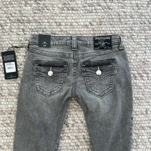 Grå bootcut jeans från True Religion - Hej!!🤗Säljer ett par jättefina och trendiga grå jeans från True Religion med bootcut passform och låg midja. Helt oanvända med prislappar kvar i modellen joey. Pris kan diskuteras! Nypris runt 1500 kr. Midjemått: 36 cm, innerbenslängd: 82cm💕