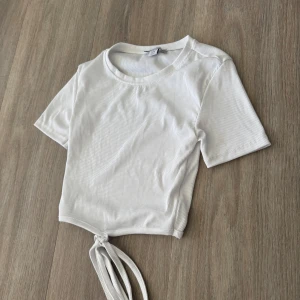 Vit ribbad croppad topp med knyt - Säljer en vit ribbad croppad topp med korta ärmar och knyt framtill. Perfekt till sommaren och enkel att matcha med jeans eller kjol. Superfräsch och trendig modell!