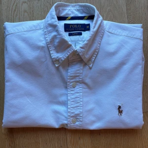 Vit skjorta från Polo Ralph Lauren - Klassisk vit skjorta från Polo Ralph Lauren i slim fit-modell. Skjortan har lång ärm, knappar framtill och broderad logga på bröstet. Perfekt till många olika stilar och enkel att matcha.