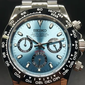 Seiko kronograf herrklocka med blå urtavla - Stilren Seiko kronograf med blå urtavla, svarta subdials och silverfärgat armband i metall. Klockan har tydliga indexmarkeringar, tachymeter-skala på bezeln och tre knappar på sidan för funktioner.
