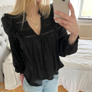 Svart v-ringad blus från Neo Noir - Säljer en superfin svart blus från Neo Noir. Blusen är v-ringad och har volanger samt hålbroderi. Sitter superfint och är perfekt för sommaren! 