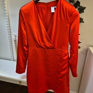 Röd satinklänning från Y.A.S - Säljer en snygg röd omlottklänning i satin från Y.A.S med lång ärm och v-ringning. Klänningen har draperad detalj i sidan och stängs med dragkedja bak. Använd vid två tillfällen så den är i nyskick. 