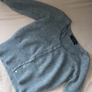 Grå kofta från Zara Knit Angora - Mysig grå kofta från Zara Knit i angora-blandning. Koftan har långa ärmar, rund halsringning och knappar framtill. Ribbstickad vid ärmslut och nederkant för extra komfort och stil.