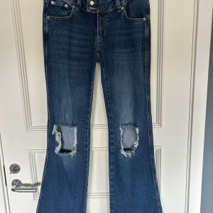 Blå bootcut jeans med slitningar - Snygga blå bootcut jeans med slitna detaljer på knäna. Jeansen har en lätt utsvängd passform nertill och är perfekta för en avslappnad stil.