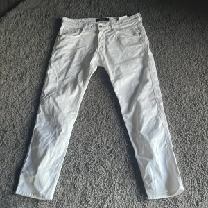 Vita jeansbyxor från Replay Anbass - Säljer ett par fräscha vita jeansbyxor från Replay, modell Anbass. Byxorna har klassisk femficksdesign, raka ben och normal passform. Perfekta för dig som vill ha en stilren och clean look. Märkesdetaljer på insidan och bak.