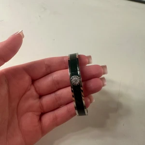 Silverfärgat armband med mörkgrön detalj från dyrberg kern - Snyggt armband i silverfärg med mörkgrön emaljdetalj och dyrberg/Kern-logga framtill. Stilren och elegant design som passar perfekt som accessoar till många olika outfits. Nypris:700kr