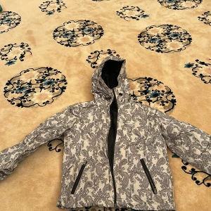 Mönstrad vindjacka med huva - Säljer en snygg vindjacka med svartvitt mönster och huva. Jackan har dragkedja framtill och två snedställda fickor med dragkedja. Perfekt för dig som vill sticka ut med en unik stil.