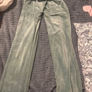 Gröna velourbyxor från Juicy Couture - Mysiga ljusgröna velourbyxor från Juicy Couture med raka ben och två fickor med lock och knappar bak. Byxorna är mellan låga och utsvängda, går att vika ner till low low rise.   Använd fåtals gånger men inte så mycket. Snöret är borttappat men det går att köpa separat på vissa ställen. Ställ frågor om du har funderingar 🫶
