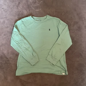 Ljusgrön långärmad tröja från Polo Ralph Lauren - Säljer en ljusgrön långärmad tröja från Polo Ralph Lauren med klassisk rund halsringning och liten broderad logga på bröstet. Perfekt för en avslappnad och stilren look.