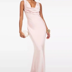 Ljusrosa långklänning med öppen rygg och snörning - Ljusrosa satinklänning som är lång med draperad urringning och öppen rygg med öppen rygg dekorativ snörning. Klänningen har en figurnära passform och är tillverkad i ett slätt, glansigt material som ger en lyxig känsla. Passar perfekt till balklänning. Klänningen har fortfarande kvar prislapp och aldrig använts 