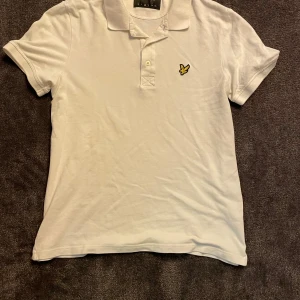 Lyle & Scott piké - Säljer en klassisk vit pikétröja från Lyle & Scott med korta ärmar och broderad gul logga på bröstet. Perfekt till sommaren och enkel att matcha med jeans eller shorts. Har du någon beundran, hesitera inte att fråga. 👍🏼 