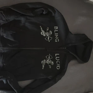 Svart hoodie med strasstenar från Bling Lucid - Hej, säljer min bling lucid Hoddie för att den har blivit för liten. Riktigt skön och snygg hoddie. Storlek XS