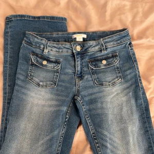 Blå jeansbyxor från Gina Tricot - Klassiska blå jeansbyxor från Gina Tricot med normal passform. Byxorna har framfickor med lock och knappar, samt vanliga bakfickor.