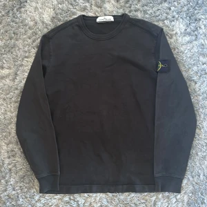 Svart långärmad tröja från Stone Island - Säljer en svart långärmad tröja från Stone Island med klassisk rund halsringning och den ikoniska loggan på vänster ärm. Tröjan är i mjuk bomull och har en stilren, enkel design som passar till det mesta.