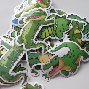 25st Krokodilklistermärken i tecknad stil - Ett set med färgglada klistermärken som föreställer olika tecknade krokodiler i gröna nyanser. Motiven visar krokodiler i olika poser och uttryck, vissa med accessoarer eller i vatten. Perfekt för att dekorera anteckningsböcker, laptops eller mobilskal.