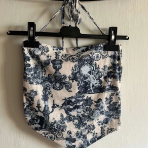 Mönstrad croppad halterneck-topp - Säljer en croppad halterneck-topp med blått och vitt barockinspirerat mönster. Toppen har knytband i nacken och spetsig nertill.