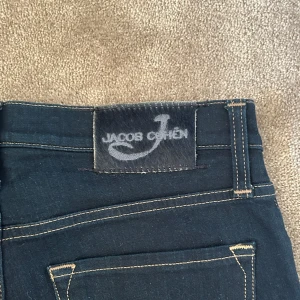 Mörkblå jeans från Jacob Cohen - Snygga mörkblå jeans från Jacob Cohen med kontrastsömmar och klassisk femficksdesign. Insidan har ett unikt mönstrat tyg och byxorna stängs med dragkedja. Perfekta för dig som gillar stilrena och exklusiva jeans. (Slimmfitt i storlek 28)
