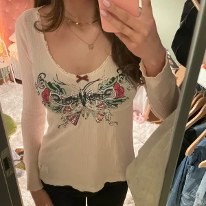 Vit ribbad långärmad topp från Odd Molly - Supersöt ljusrosa ribbad topp från Odd Molly med lång ärm och djup rundad urringning. Framsidan har ett stort färgglatt tryck med rosor, fjäril och texten 'break free', samt en liten rosett vid halsen. 