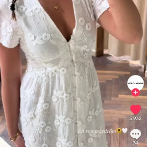 Vit blommig klänning från Vero Moda - Superfin vit klänning från Vero Moda med broderade blommor och v-ringning. Klänningen har korta ärmar, knappar framtill och en romantisk känsla med fina spetsdetaljer. Perfekt för sommarens alla tillfällen som midsommar!