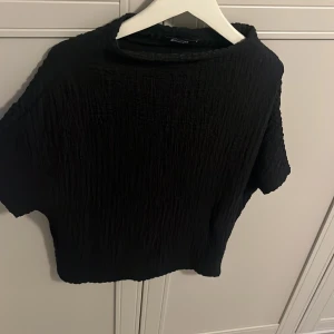 Svart kortärmad topp med struktur - Säljer en svart topp med korta ärmar och snyggt strukturerat tyg. Modellen är elegant passar perfekt till både jeans och kjol. Enkel och stilren design som är lätt att matcha.