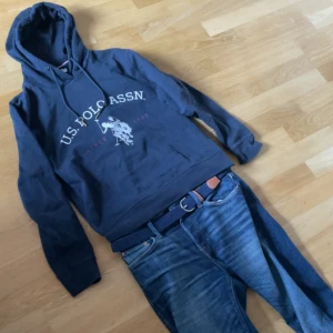 Mörkblå hoodie från U.S. Polo Assn. Ralph Lauren  - Säljer en mörkblå hoodie från U.S. Polo Assn. med vit logga och tryck framtill. Tröjan har huva med dragsko. Perfekt för dig som gillar sportig och avslappnad stil.