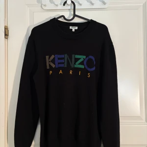 Svart sweatshirt från Kenzo - Säljer en svart sweatshirt från Kenzo med färgglad broderad logga på bröstet. Tröjan har rund halsringning och långa ärmar. Perfekt för dig som gillar streetwear och vill ha något stilrent men ändå med en twist.