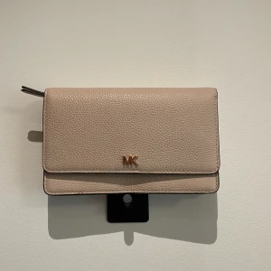 Beige/ljus rosa plånbok från Michael Kors - Säljer en stilren beige plånbok från Michael Kors i skinn med guldfärgad MK-detalj framtill. Plånboken har flera kortfack, dragkedjefack och tryckknappsstängning. Perfekt för att hålla ordning på kort och kontanter. Aldrig använd, köpt för 1200:- och säljs nu för 450:- 