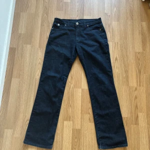 Svarta bootcut jeans med broderade bakfickor - Snygga svarta jeans med bootcut passform. Bakfickorna har ett broderat mönster och små nitar som detalj. Klassisk femficksmodell med knapp och dragkedja framtill. Perfekta för dig som vill ha en stilren men ändå unik look.