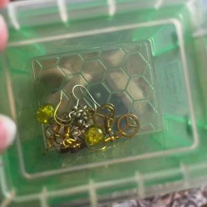 Mixade örhängen med olika motiv och färger - Säljer ett gäng unika örhängen i olika stilar. Här finns bland annat örhängen med peace-symbol, blommor och glittrande gula pärlor samt andra coola hängen i guld och silver. Perfekt för dig som gillar att mixa och matcha smycken!