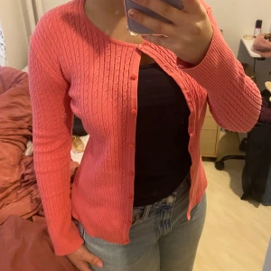 Rosa ribbad kofta med knappar - Säljer en söt rosa kofta med ribbat mönster och knäppning framtill. Koftan har långa ärmar och en smickrande passform. Perfekt att slänga över en topp till jeans för en enkel men snygg look.